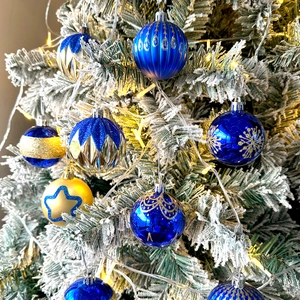 Close-up of blue and gold Christmas ball ornaments with glitter details on a snowy pine branch