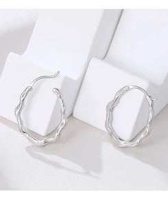 Macro shot of silver 925 hoop earrings with irregular wave texture on white pedestal