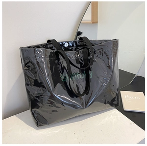 Detail of a large black glossy tote bag featuring green Skillful text print and chic handles