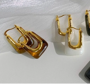 Detailed view of U-shaped resin earrings in amber and ivory on white fabric