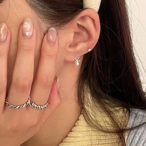Macro detail of silver bow pearl earrings and vintage twisted rope texture rings