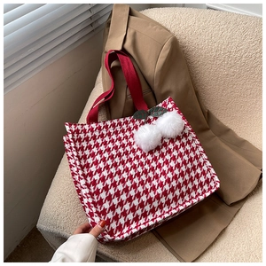Detail of red houndstooth tote bag featuring plush cherry charm and woven texture