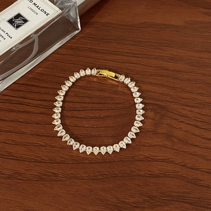 Detail of elegant gold bracelet featuring pear-cut cubic zirconia on a dark wood surface