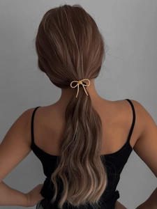 Detail of a gold metallic bow hair tie with textured finish on a ponytail
