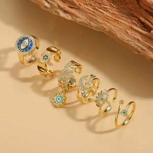 Set of 6 gold rings with evil eye, flower, and star designs on elegant wood display