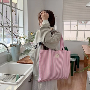 Close-up of pink and white striped canvas tote bag with brand label in lifestyle setting