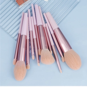 Mise à plat de 11 pinceaux maquillage roses avec viroles or rose sur fond bleu clair