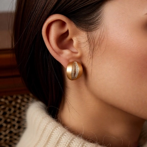 Detailed view of C-shaped gold studs with zircon rows on matte metallic surface