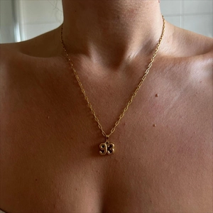 Close-up of model wearing gold necklace with 93 year pendant and paperclip chain