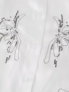 Detailed close-up of grey beaded butterfly embroidery on a white silk satin shirt