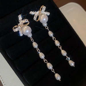 Detailed macro of rhinestone bow earrings with long water drop pearl tassels on black velvet