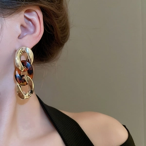 Detail of amber tortoiseshell acrylic and gold chain earrings on model with knit top