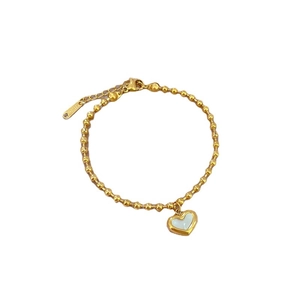 Golden titanium steel beaded bracelet with white mother-of-pearl heart charm on white background