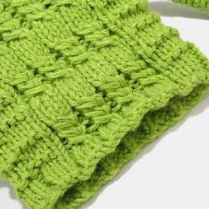 Detailed macro view of grass green chunky knit fabric with ribbed cuff and waffle texture