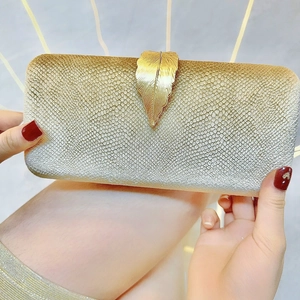 Close-up of golden leaf metal clasp and glitter texture on an elegant evening clutch bag