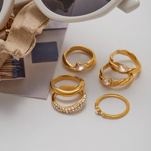 Five-piece gold stainless steel ring set with zircon accents on a textured fabric background