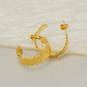 Close-up of golden geometric ribbed C-hoop earrings with polished metallic texture