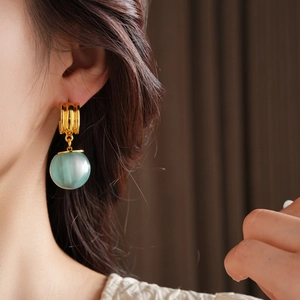Detail shot of a minimalist gold ear stud with a mint green resin ball pendant