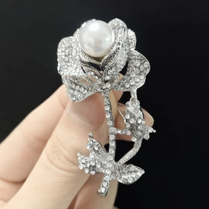 Detailed view of a silver rose brooch with sparkling rhinestones and a large center pearl