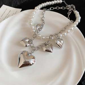 Detail of a pearl and silver metal chain necklace featuring diverse heart-shaped pendants