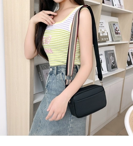 Detail of black pebbled leather crossbody bag with striped wide shoulder strap worn by model