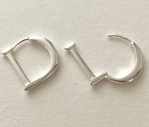 Macro view of silver-tone D-shaped minimalist hoop earrings on textured beige paper