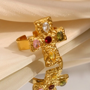 Macro shot of 18K gold-plated cross ring with colorful gems on beige silk with reflection