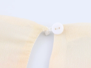 Dettaglio dello scollo a V con bottone bianco su un abito floreale in chiffon giallo