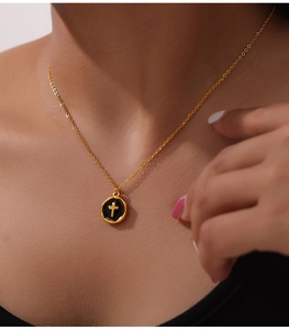 Detail view of a gold chain necklace with a black enamel round pendant and golden cross