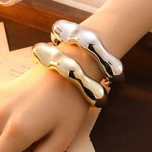 Close-up of chunky wave-shaped gold and silver bangles worn on a model's wrist