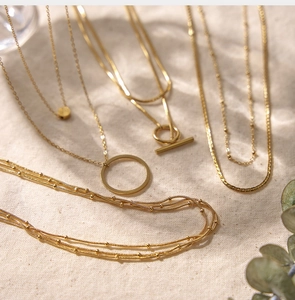 Detail of layered 18K gold-plated necklaces with O-chain and OT buckle on beige fabric