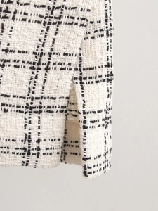 Close-up of black and white plaid tweed fabric showing the detailed split hem craftsmanship