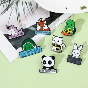 Close-up of colorful enamel animal pins with humorous slogans on a green surface