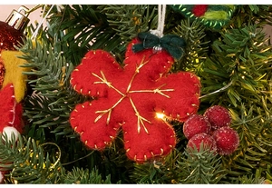 Detail of red wool felt snowflake ornament with gold embroidery on Christmas tree branches