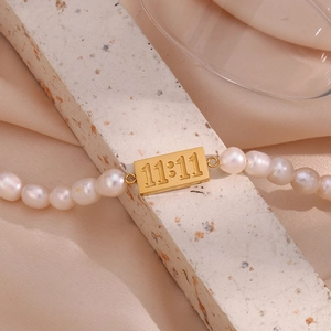 Detailed macro of 11:11 rectangular gold plaque on elegant white freshwater pearl bracelet