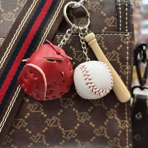 Detail of red leather glove, mini baseball, and wood bat pendant on a patterned bag