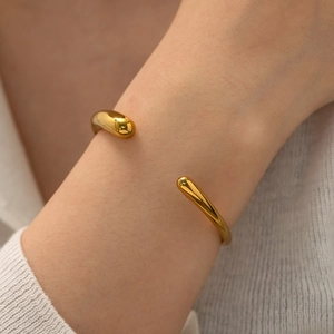 Close-up of golden minimalist open bangle with smooth finish on a female wrist