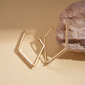Gold geometric rhombus earrings with sparkling crystals on a textured warm background
