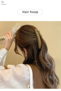 Detailed side view of a large matte beige banana hair clip on wavy brown hair