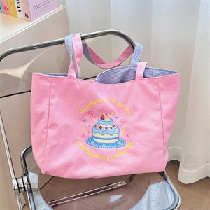 Close-up of pink canvas tote bag featuring cake embroidery and blue checkered lining