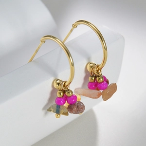 Detail of 14k gold C-shape earrings with vibrant beads and natural stones on white stone