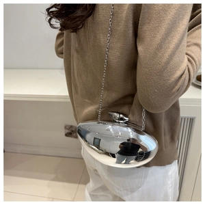 Silver mirror-finish oval clutch bag with thin chain strap worn by a model