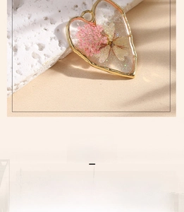 Detail of heart-shaped resin pendant with pink dried flowers and golden metal frame