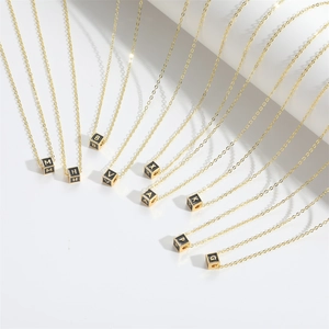 Gold chain necklace with black enamel cube alphabet pendant on a white background