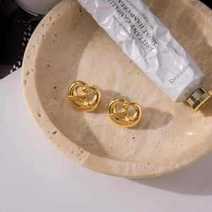 Detail of gold-plated stainless steel pretzel heart earrings on a natural stone tray