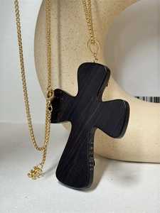 Detailed view of large dark resin cross pendant with an elegant gold chain on a prop