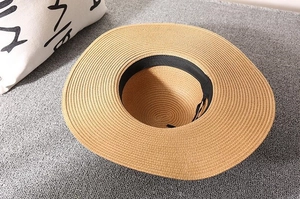 Detailed top view of wide brim straw hat with black inner sweatband on textured grey surface