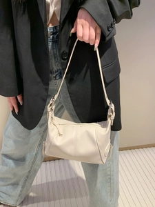 White minimalist leather shoulder bag with side zipper detail worn by a model