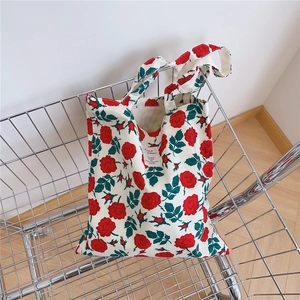 Detailed view of white canvas tote bag featuring red rose prints in a shopping basket