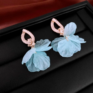 Detailed close-up of light blue acrylic flower earrings with zircon studs on black tray